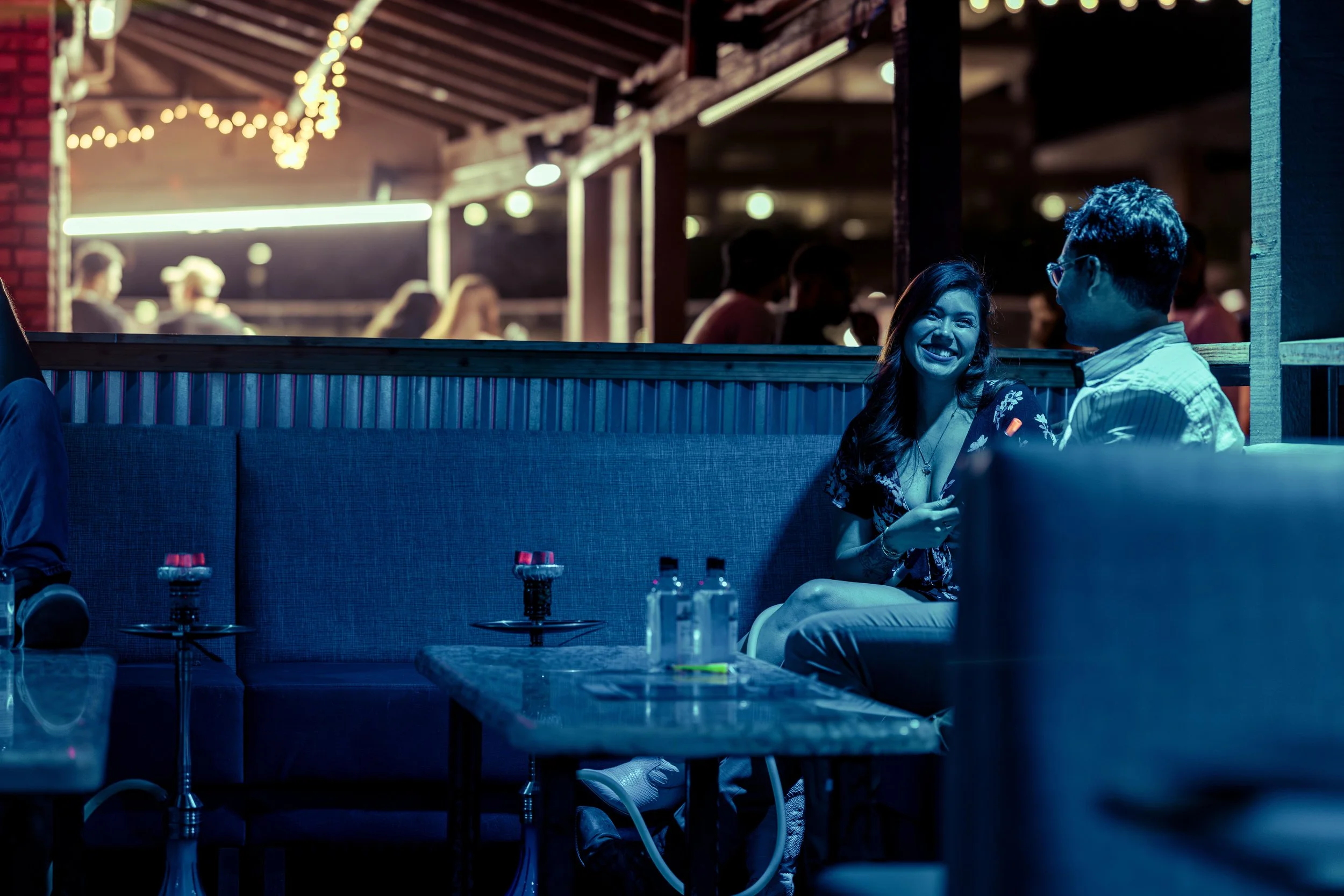 Two guests sharing a laugh in a booth at Oasis beneath glowing string lights