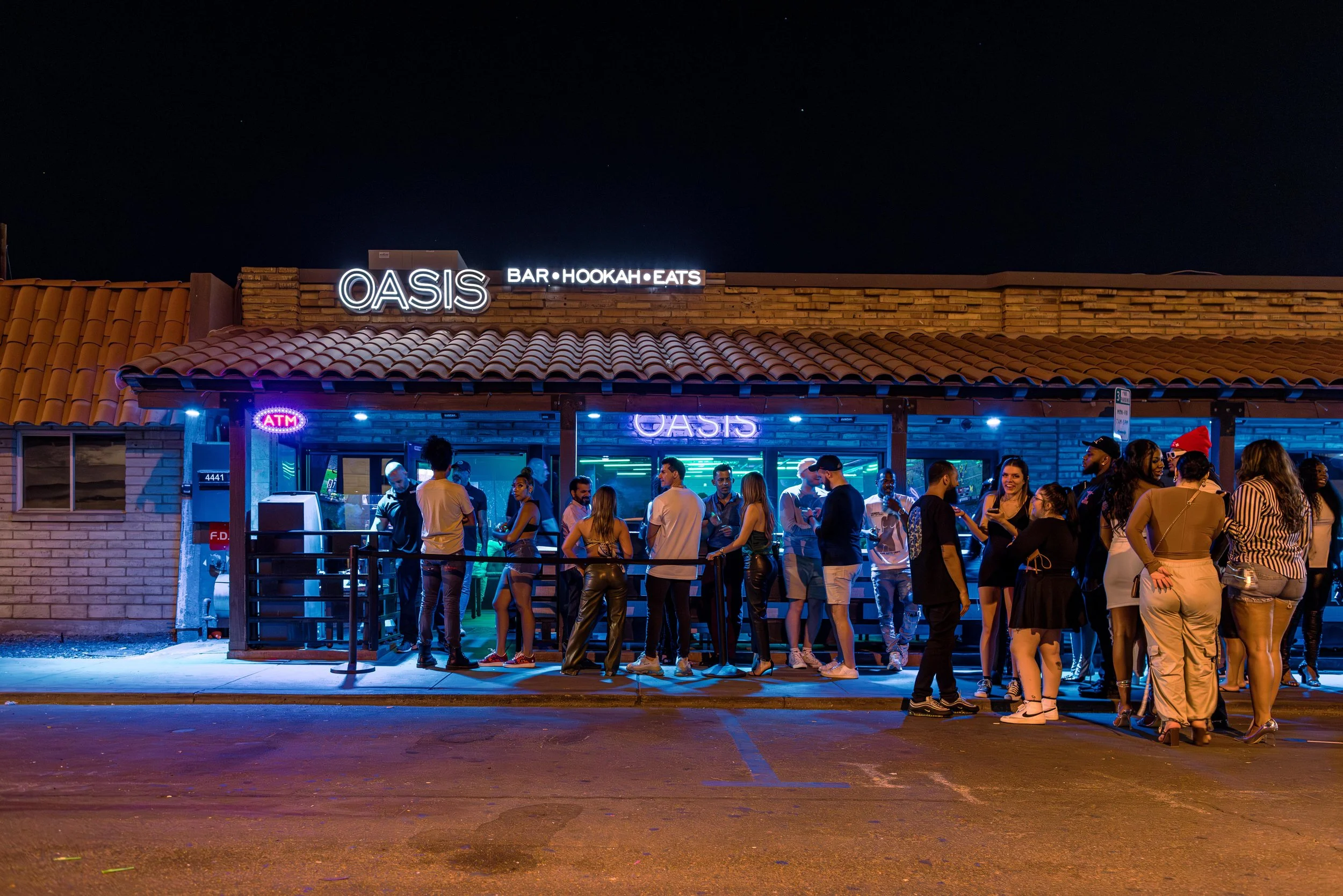The glowing Oasis storefront on Buckboard Trail with guests gathered outside at night